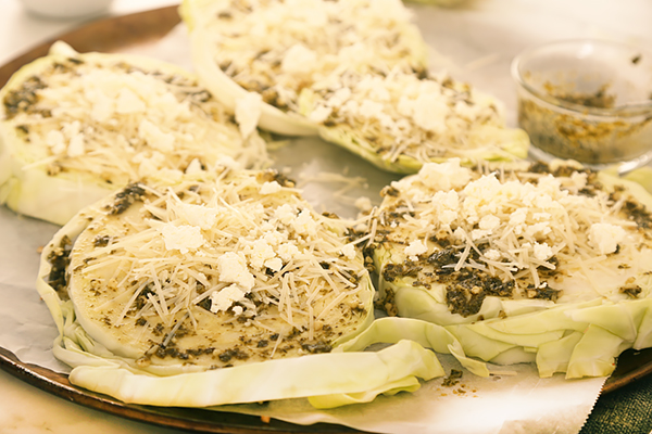 Thick cabbage steaks spread with pesto and topped with parmesan and feta on a sheet pan