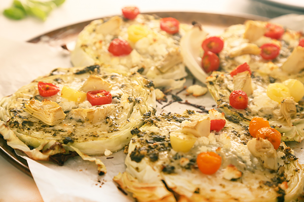 Cabbage steaks loaded with pesto, cherry tomatoes, artichoke hearts, and feta before roasting