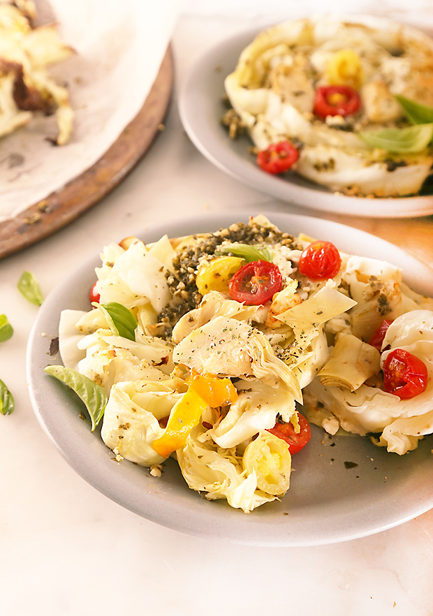 Roasted cabbage steak with blistered cherry tomatoes, artichoke hearts, and fresh basil on a plate
