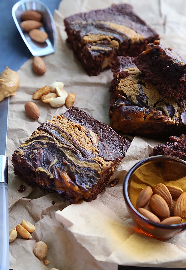 Sliced peanut butter swirl brownies with fudgy centers on parchment paper beside whole almonds