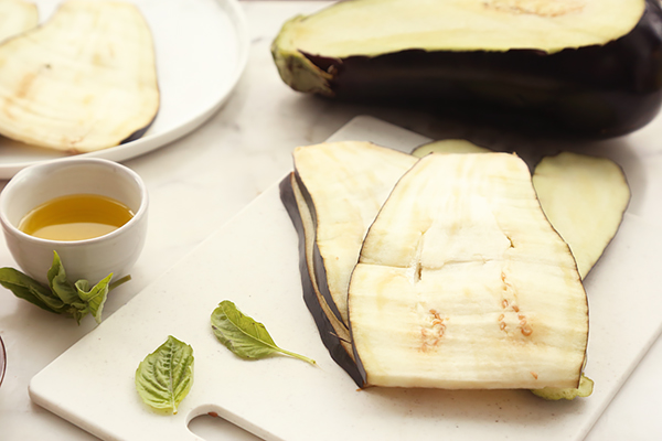 Eggplant sliced into thin lengthwise planks on a white cutting board with olive oil