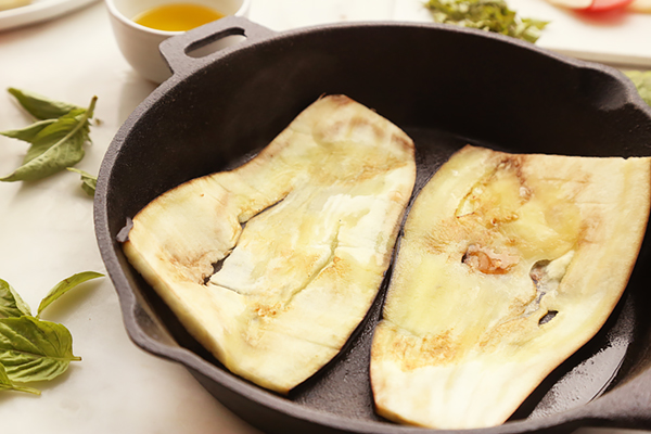 Two eggplant slices grilling in a cast iron skillet brushed with olive oil