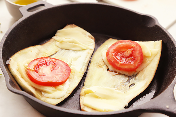 Grilled eggplant slices topped with mozzarella and tomato rounds in a cast iron skillet