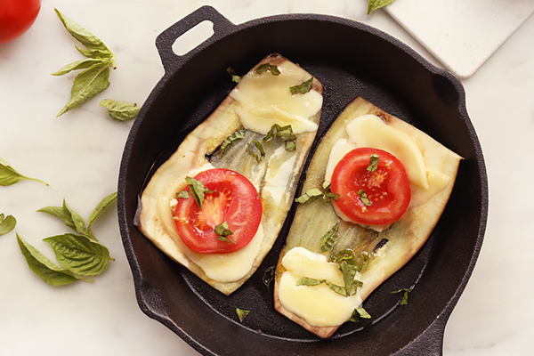 Fresh basil scattered over melted mozzarella and tomato on grilled eggplant in a nonstick pan