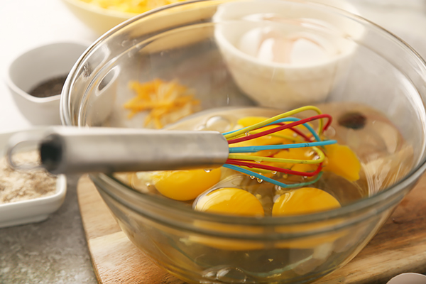 Whole eggs cracked into a glass mixing bowl with a colorful whisk
