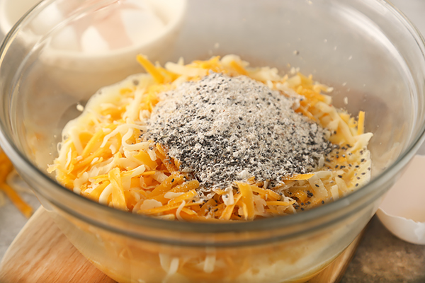 Shredded cheddar cheese and dry mix added to beaten eggs in a glass bowl