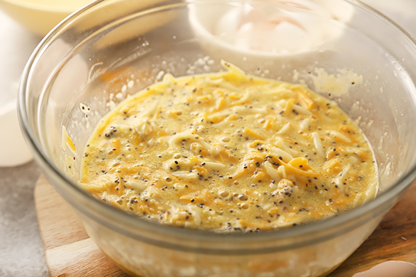 Cheese bun batter with visible chia seeds and shredded cheddar rising in a glass bowl