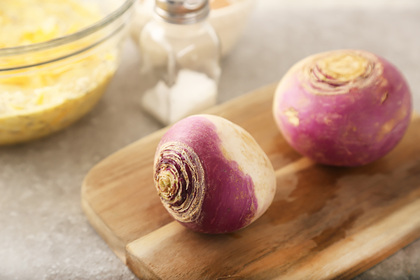 Two whole rutabagas with purple and cream skin on a wooden the board