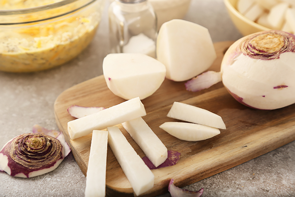 Peeled rutabaga cut into thick fry-shaped sticks on a wood board
