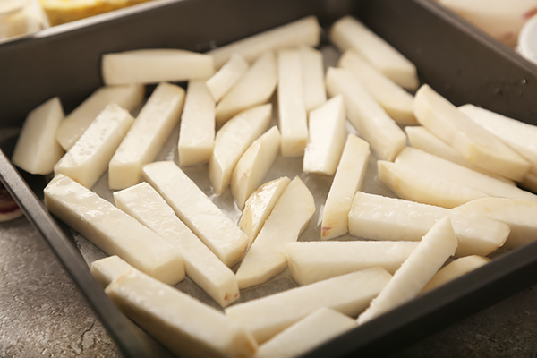 Oil-coated rutabaga fries spread in a single layer on a dark baking pan