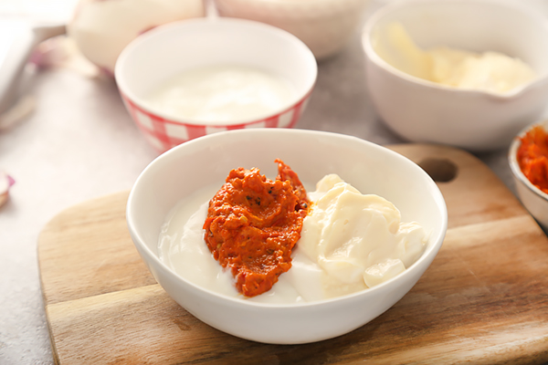 Oven-roasted red pepper puree, sour cream, and mayonnaise in a white bowl before stirring