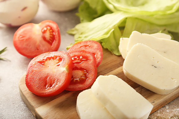 Sliced tomatoes and thick-cut halloumi cheese on a board with iceberg lettuce behind