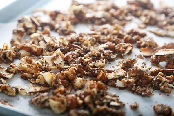 Granola mixture spread across a parchment-lined baking sheet with visible cinnamon