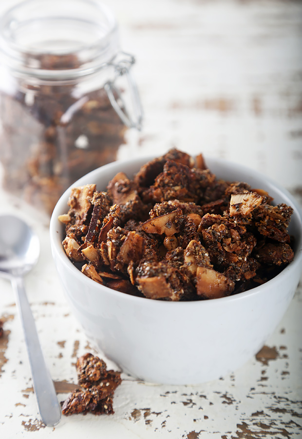Crunchy baked coconut granola broken into clusters in a white bowl beside a glass jar