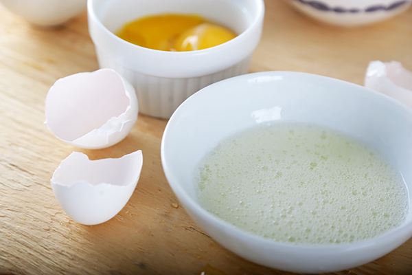 Separated egg white in a white bowl with yolk reserved in a ramekin behind