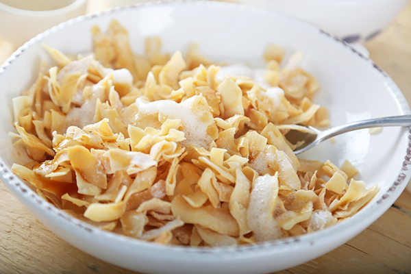 Stirring egg white and erythritol coating into toasted coconut flakes in a bowl