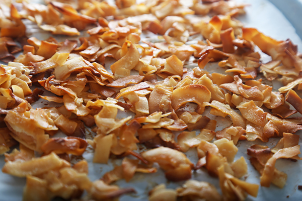 Baked coconut flakes turning deep golden on the baking sheet after stirring