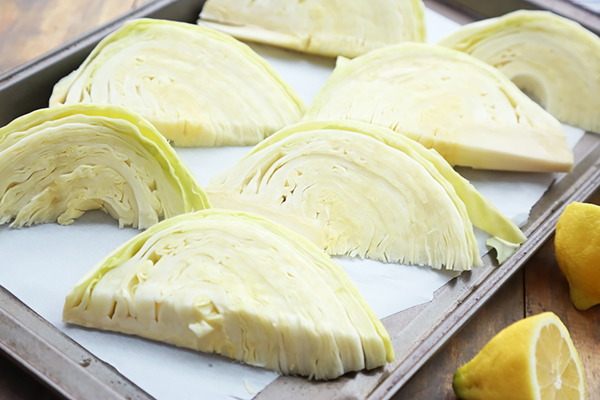 Eight green cabbage wedges arranged on a parchment-lined baking sheet