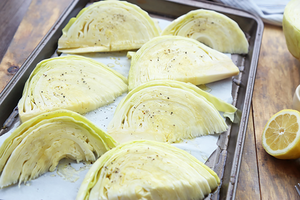 Cabbage wedges brushed with olive oil and seasoned with salt and pepper on a baking sheet