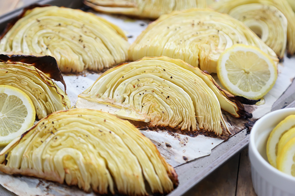 Roasted cabbage wedges with browned caramelized edges and lemon slices on a sheet pan