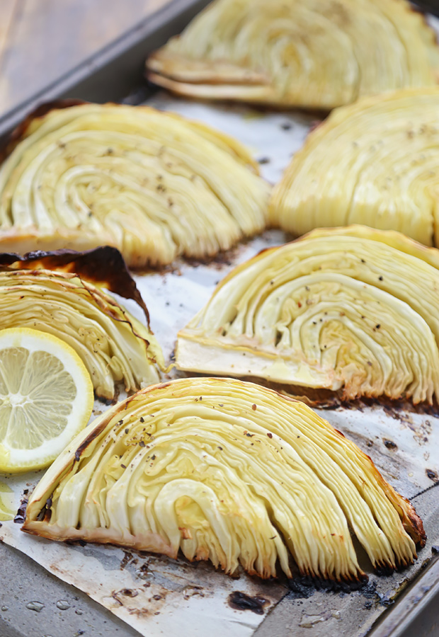 Deeply caramelized roasted cabbage wedges with charred edges and a lemon slice on parchment