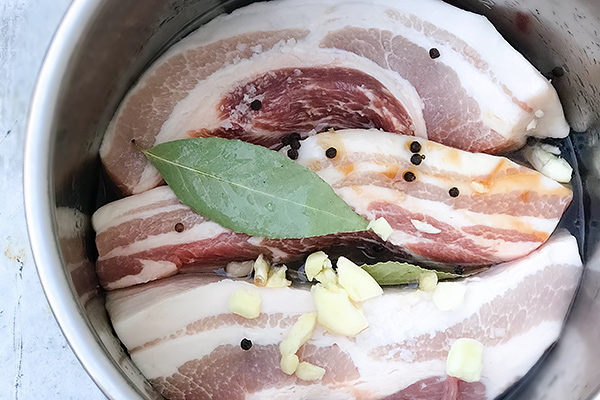 Pork belly slabs layered in a pressure cooker with garlic, bay leaf, and peppercorns
