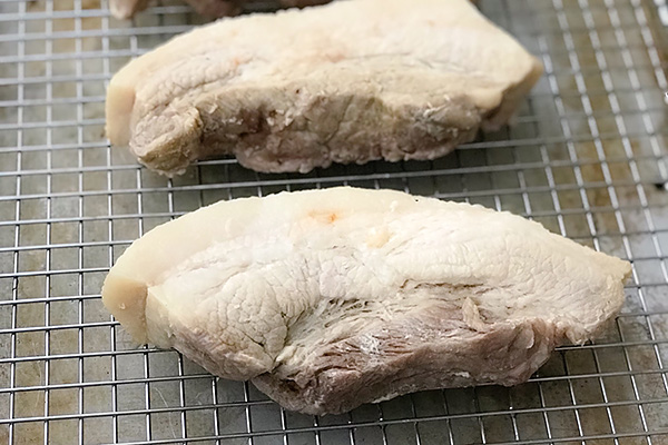 Cooked pork belly slabs drying on a wire rack after pressure cooking
