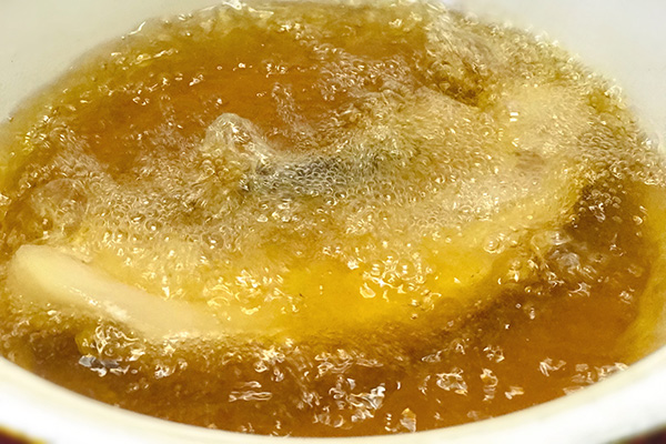 Pork belly deep-frying in hot bubbling lard in a heavy pot