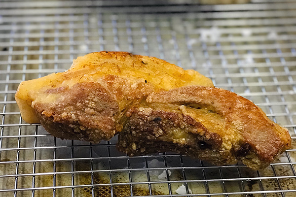 Golden fried pork belly draining on a wire rack after the first fry