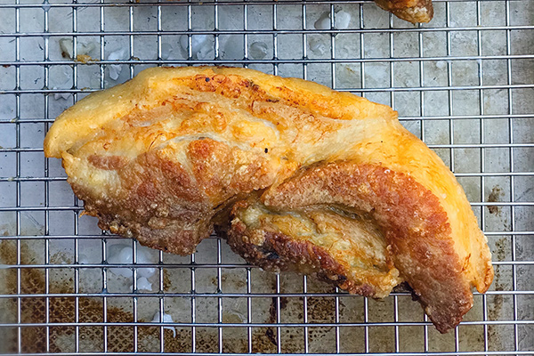 Double-fried pork belly with puffed skin resting on a wire rack