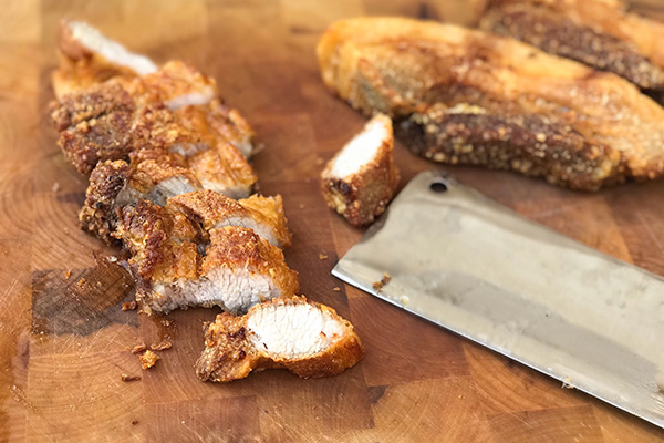 Slicing lechon kawali into thick pieces on a wooden cutting board