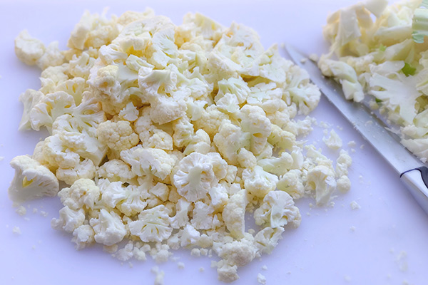 Finely chopped cauliflower florets on a white cutting board with a knife
