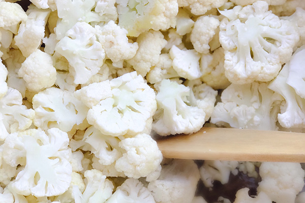 Cauliflower pieces sauteing in butter with a wooden spoon in a pot