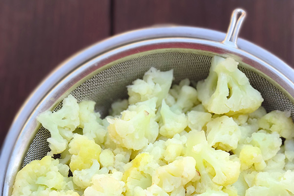 Tender boiled cauliflower draining in a fine mesh strainer
