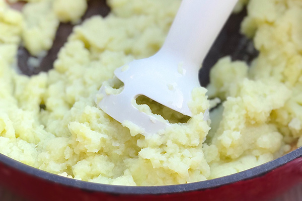 Mashing cauliflower with a potato masher in a red pot