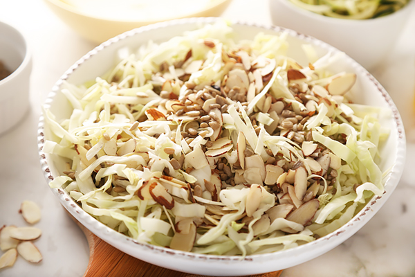 Spiralized zucchini, shredded cabbage, sliced almonds, and sunflower seeds tossed in a prep bowl
