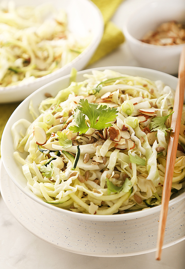 Dressed zucchini noodle and cabbage salad topped with almonds and cilantro, chopsticks resting on the bowl