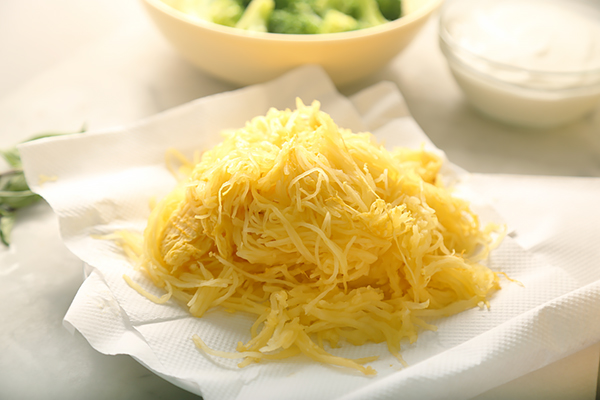 Strained spaghetti squash strands drying on paper towels with broccoli and sour cream behind