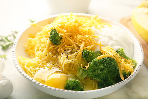 Spaghetti squash, broccoli, shredded cheddar, sour cream, and egg in a mixing bowl