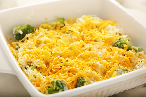 Broccoli and spaghetti squash mixture topped with shredded cheddar in a white casserole dish