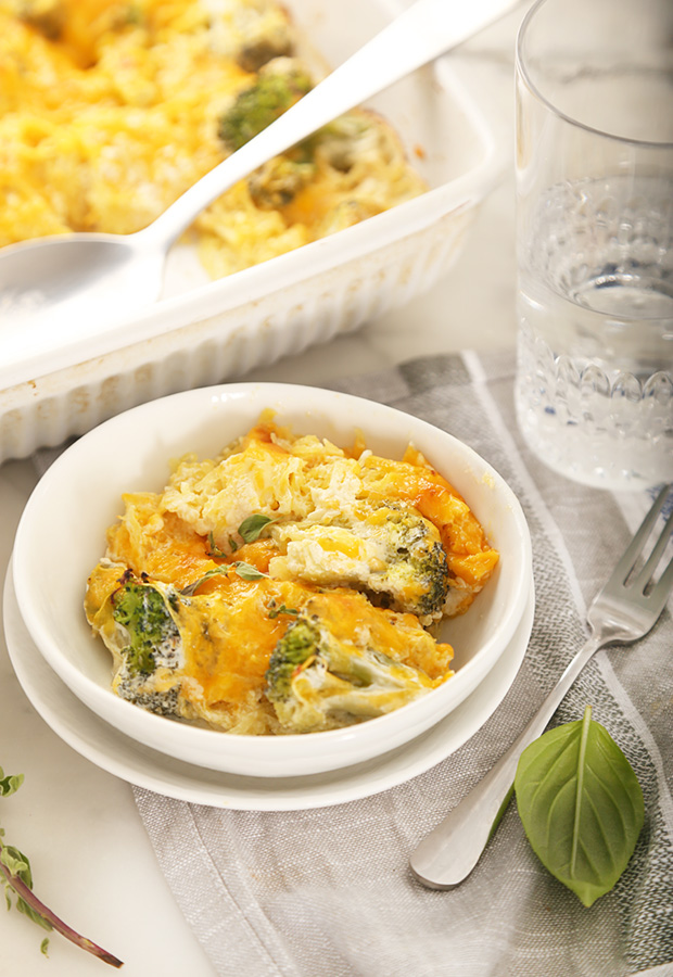 Baked broccoli cheddar casserole served in a small white bowl with fresh herbs