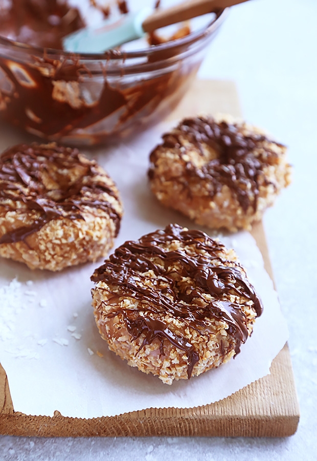 Toasted coconut samoa donuts with dark chocolate drizzled across the tops on a wooden board