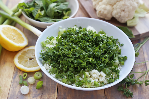 Finely chopped parsley, mint, and green onion scraped over riced cauliflower in a white bowl