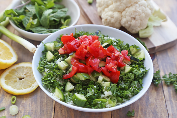 Diced cucumber and tomato piled on chopped parsley and cauliflower rice in a white bowl