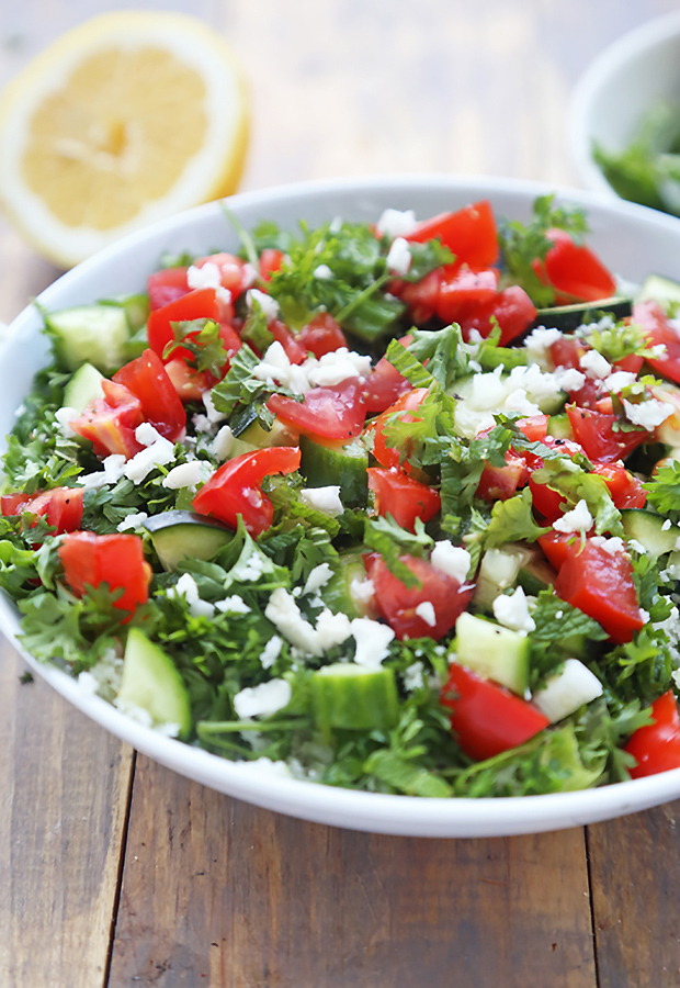 Cauliflower tabouli tossed with tomato, cucumber, parsley, and crumbled feta in a white bowl