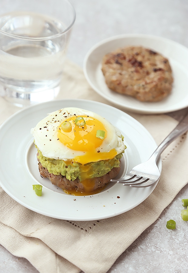 Breakfast stack with a sausage patty, guacamole, and runny fried egg on a white plate