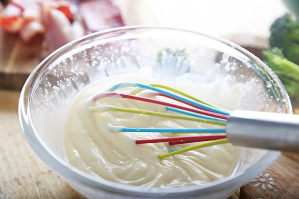 Whisking mayonnaise, erythritol, and apple cider vinegar into a smooth dressing in a glass bowl