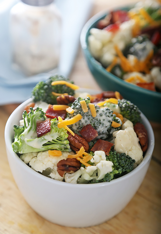 Broccoli and cauliflower salad tossed with bacon, shredded cheddar, and pecans in a large bowl