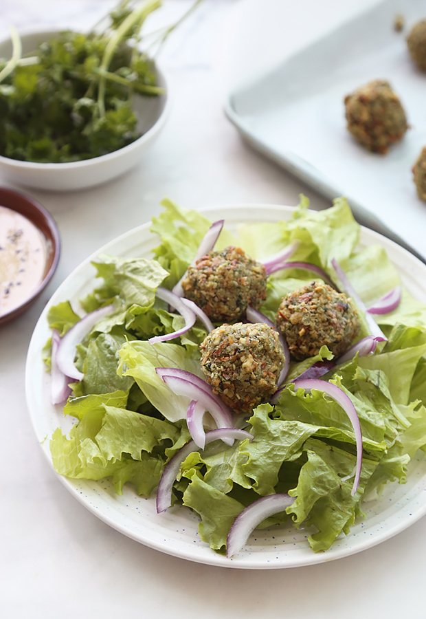 Three keto falafel on a bed of lettuce with red onion rings and dipping sauce