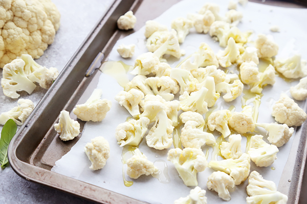 Raw cauliflower florets spread on a parchment-lined baking sheet drizzled with olive oil